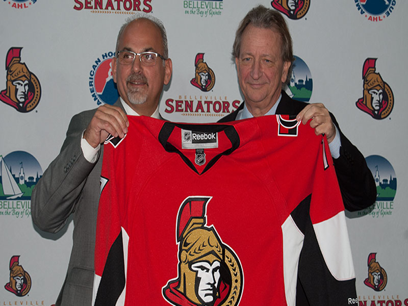 Mayor Taso Christopher and Ottawa and Belleville Senators owner Eugene Melnyk hold up a Senators' jersey at a press conference where both announced minor hockey would be returning to Belleville. Photo by Matthew Murray, QNet News.